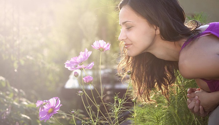 Young beautiful woman smells a flower in the garden
